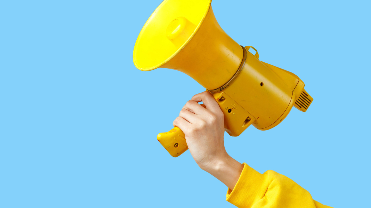 a girl's hand in yellow clothes holds a yellow megaphone on a blue background.